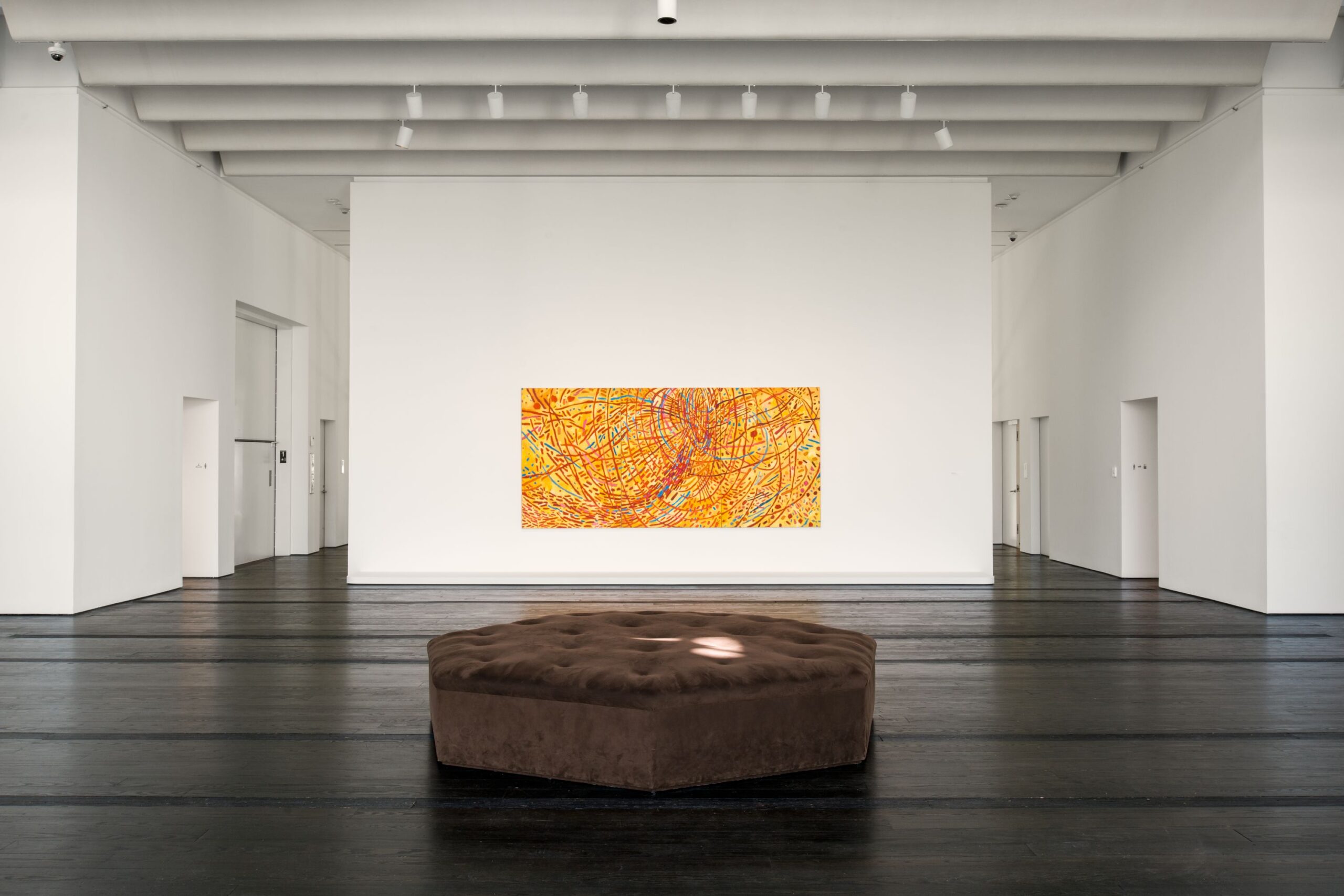 Image of a yellow, red, and blue painting on a white wall in a large gallery space with white walls and black flooring.