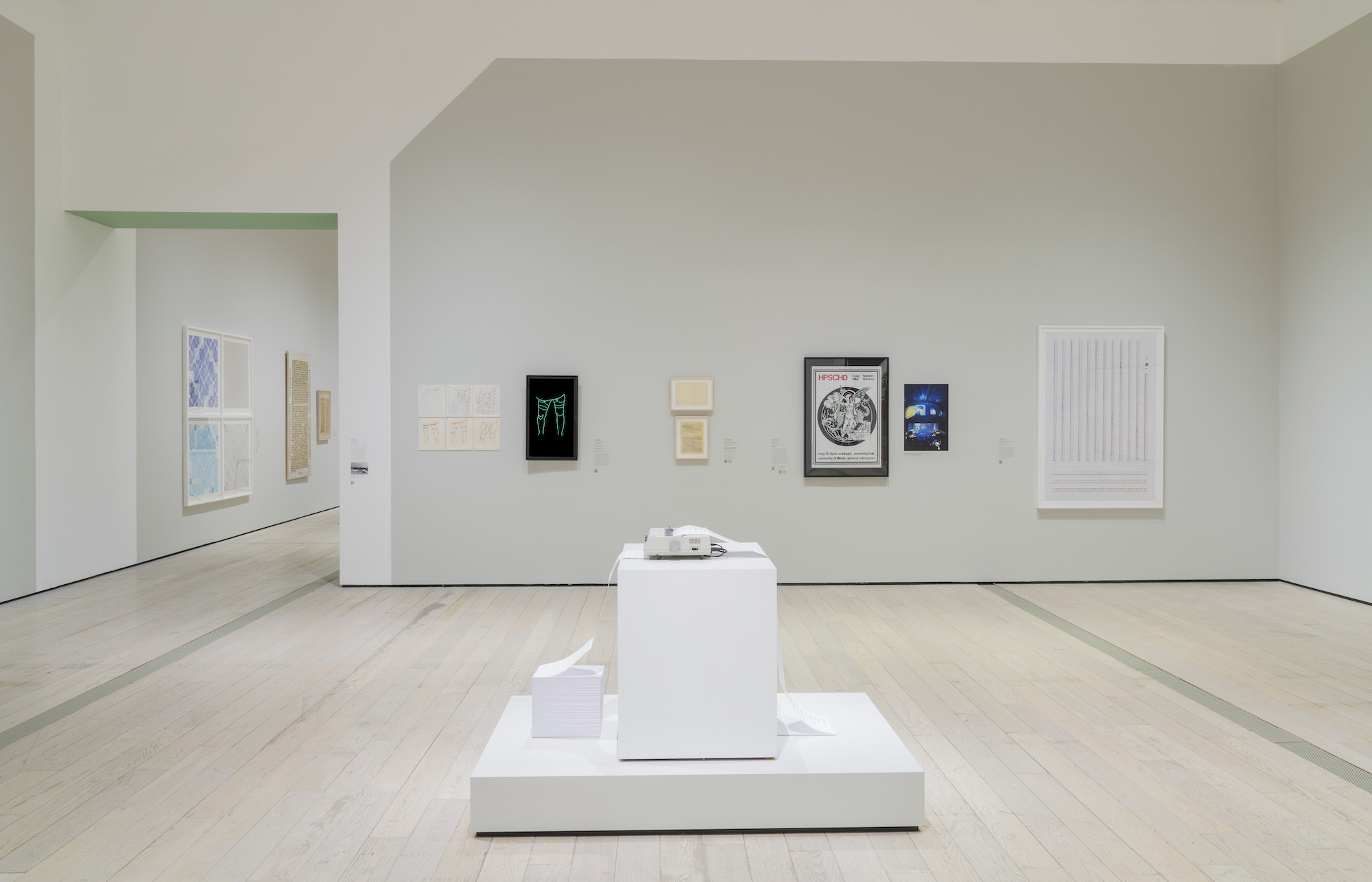A view of this sterile museum with white walls, white pedestals and framed pieces in the background.