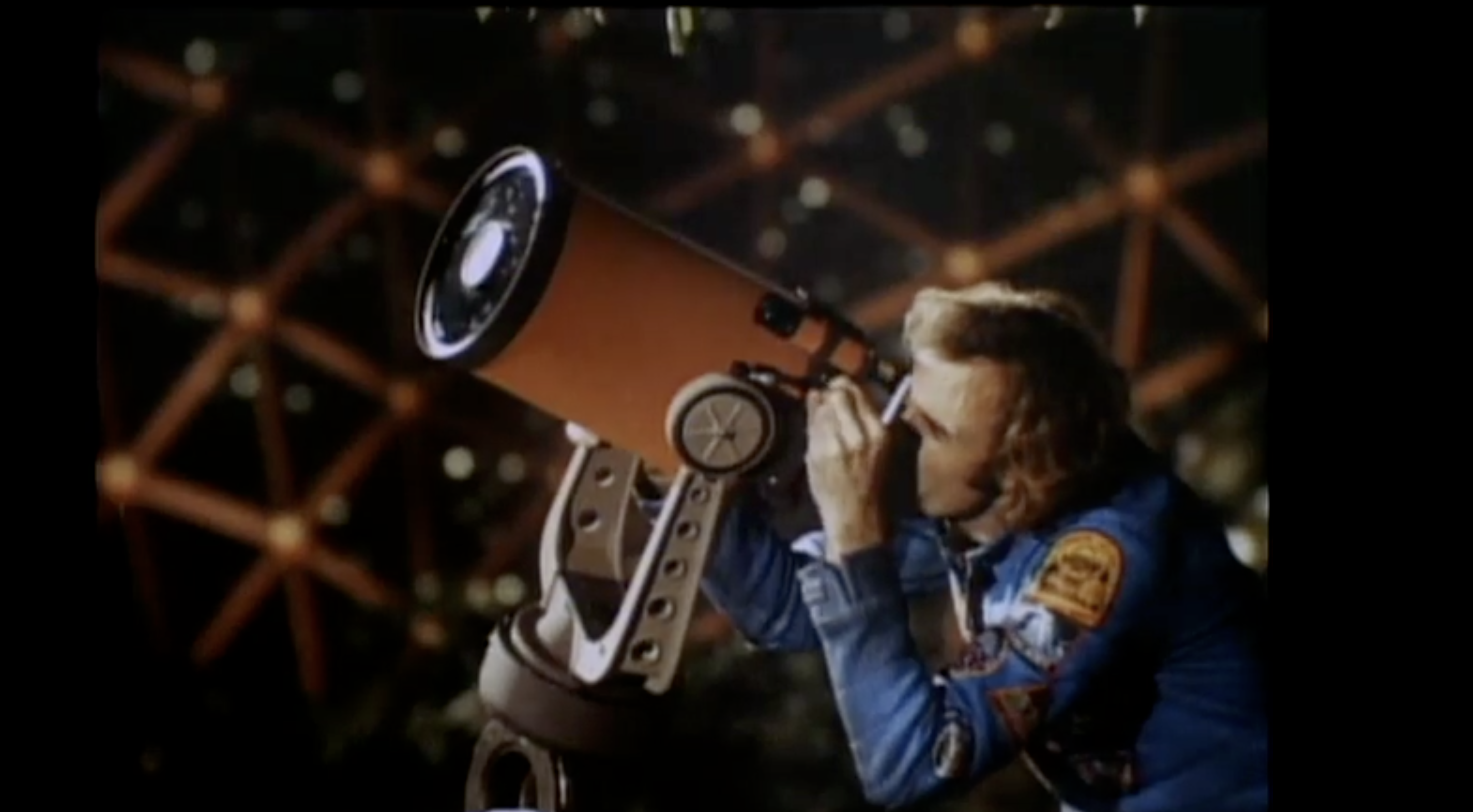 A screenshot of a video depicting a man looking at the sky through a telescope in front of a background of dome.