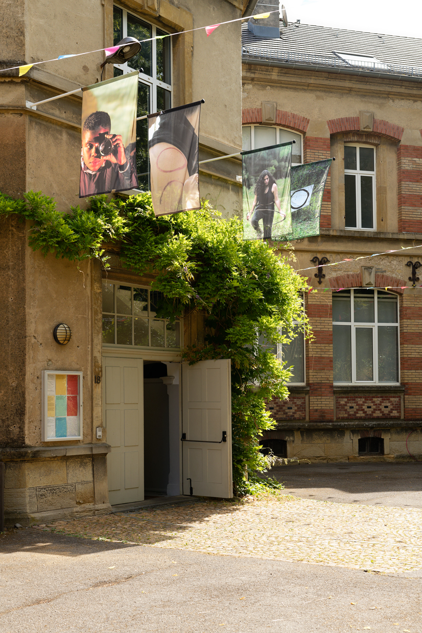 A lush entrace of CRAC Alsace is surrounded by hanging plants amongst old buildings.