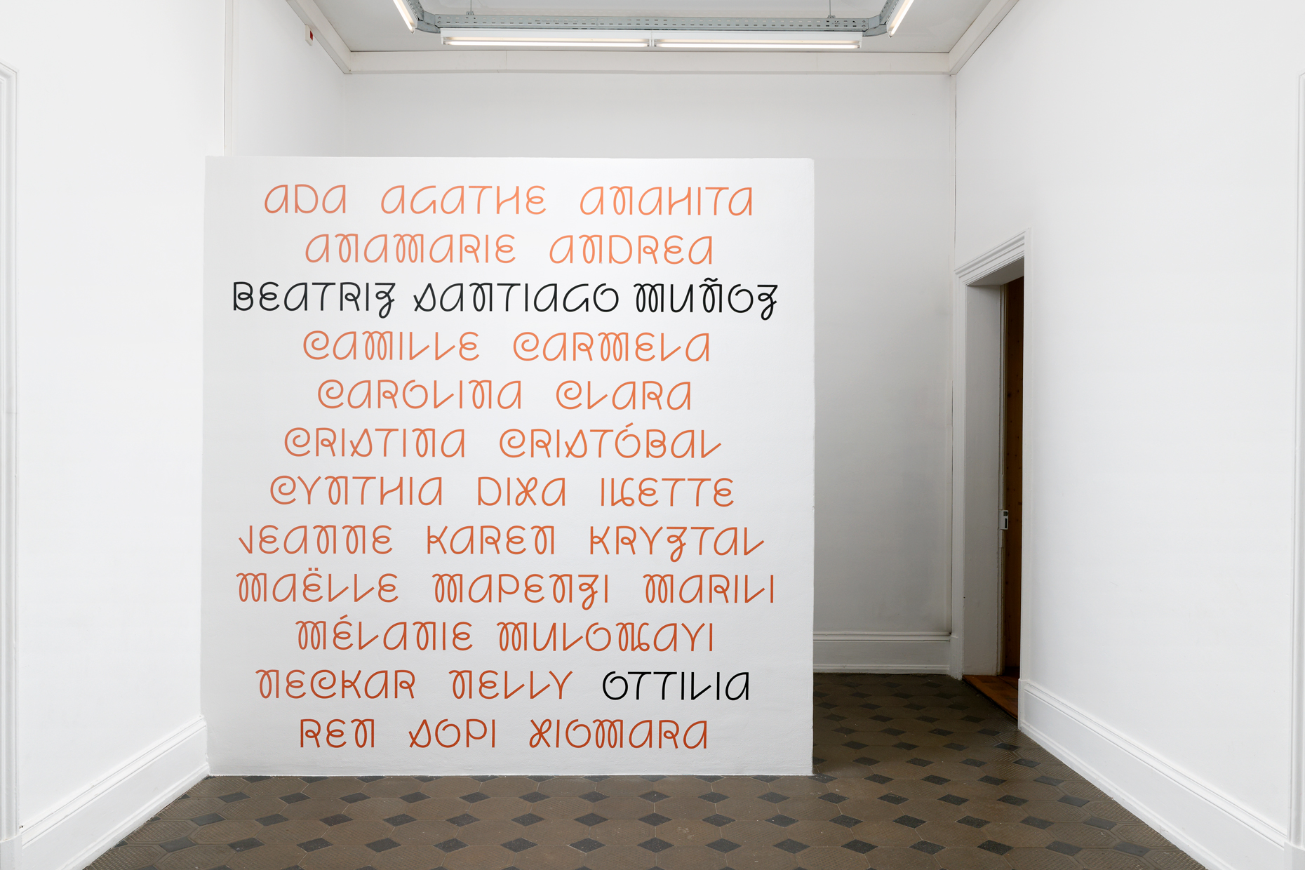 A large wall within the exhibition is decoratively adorned with the names of participants and of the artist acting as a credits for those whose work and contribution is shown with their names in orange and the exhibition title and artist's name in black.