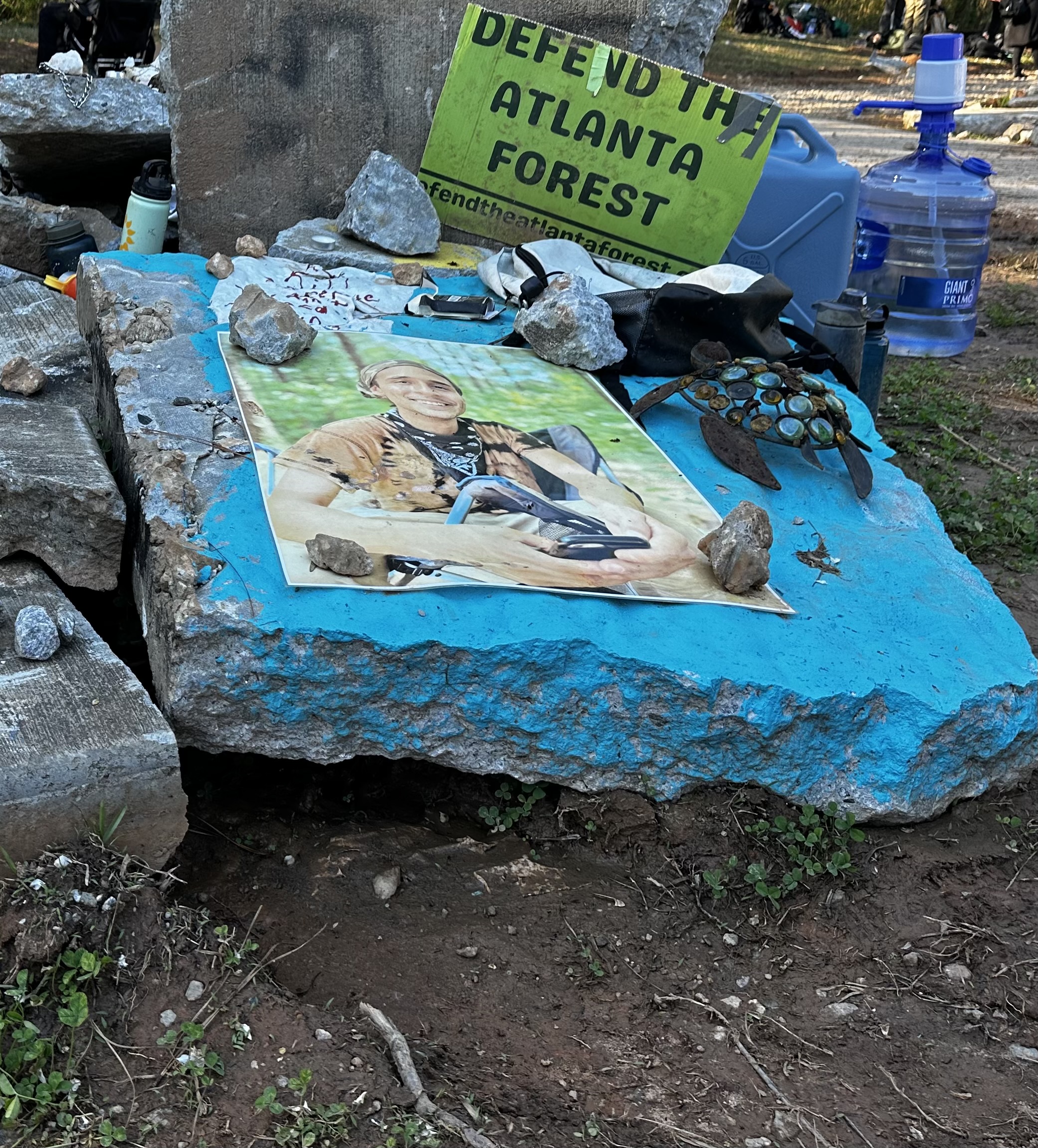 A concrete slab among a pile of slabs is painted blue with the photograph memorializing slain environmental activist, Tortuguita