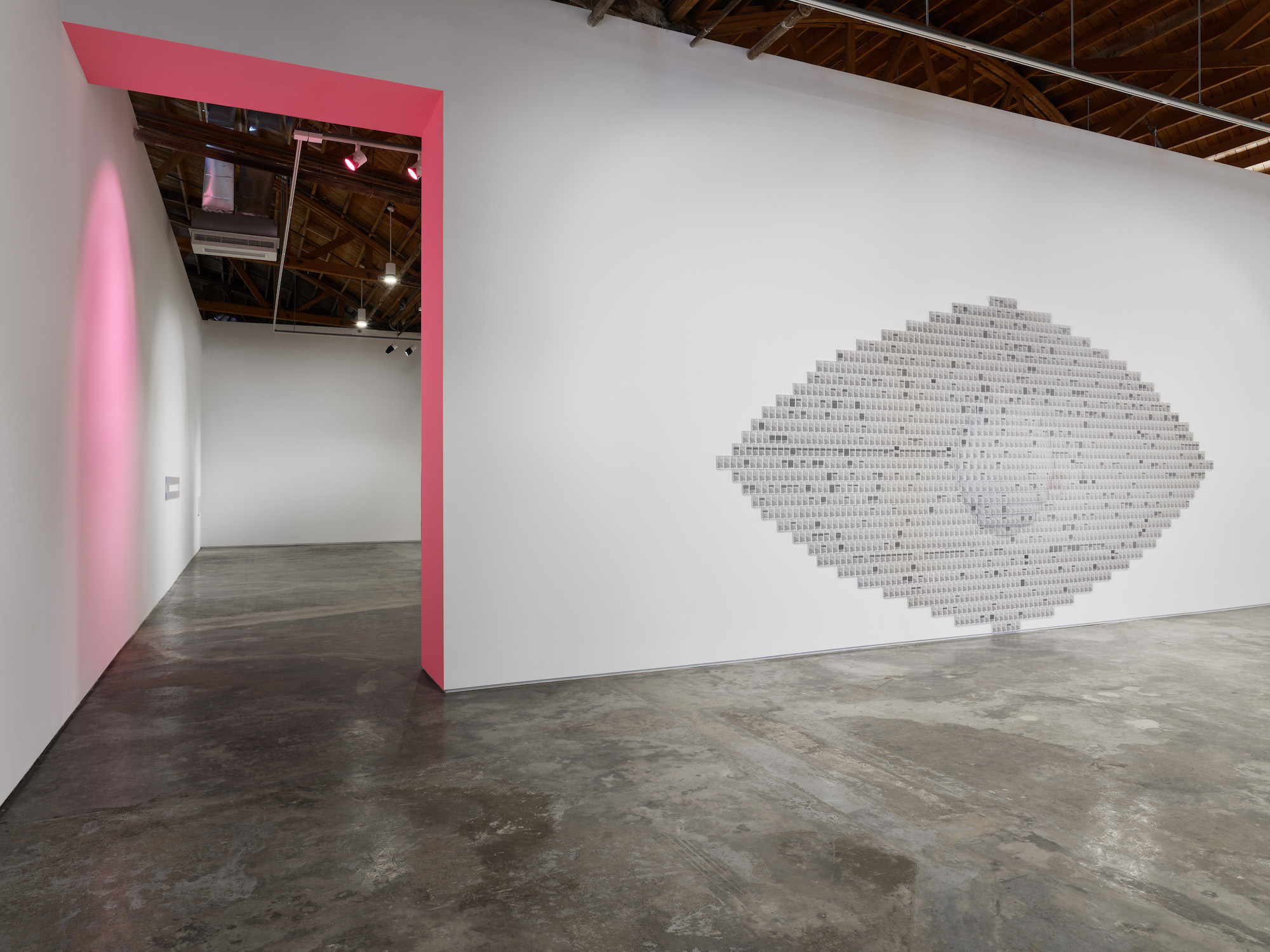 A pink strip of wall and ceiling connect two rooms of the gallery with a large eye made of dozens of tiny images hangs to the right.