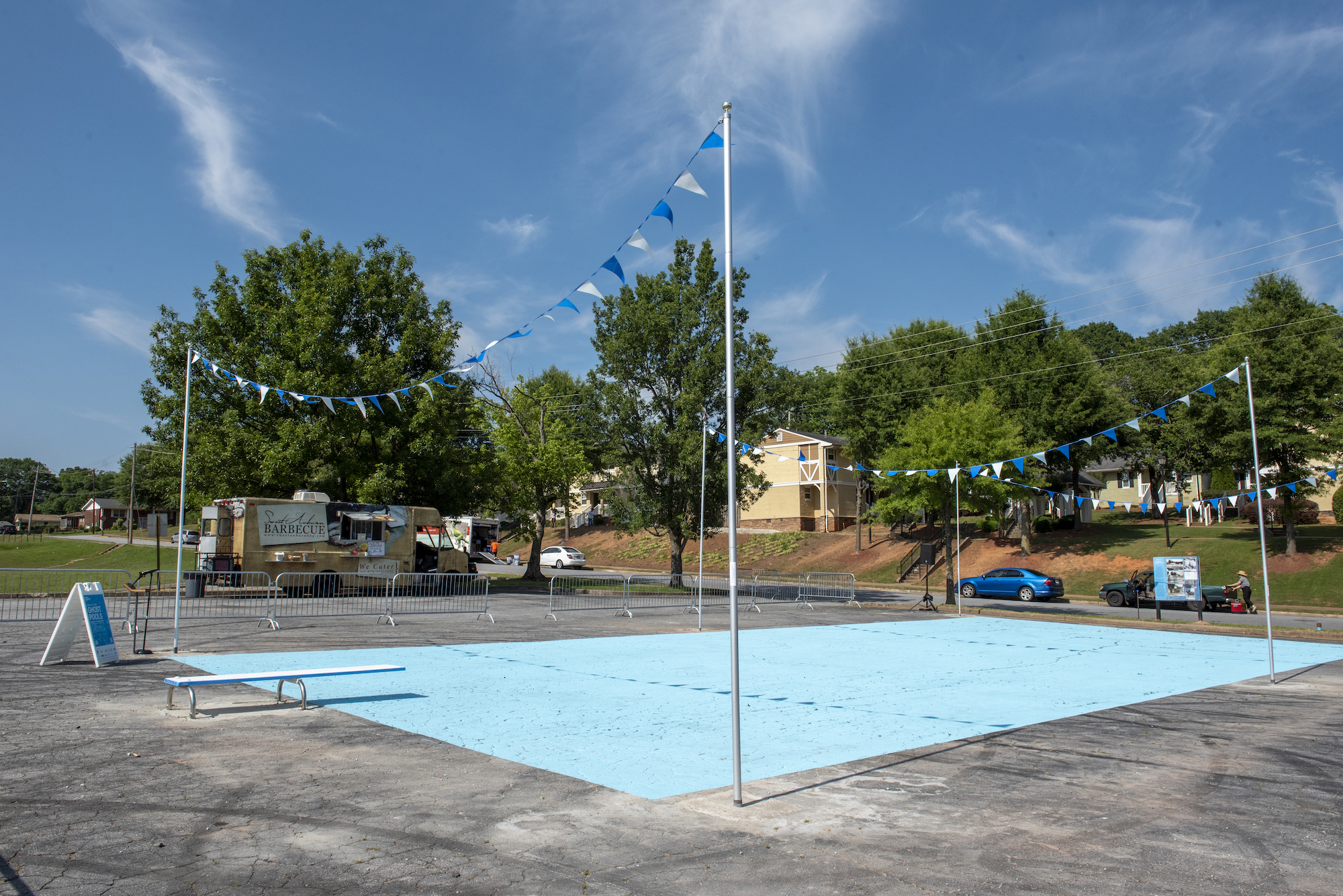 A giant rectangle within a parking lot is painted light blue with a diving board at one end and poles and streamers around the perimeter on a bright sunny day.