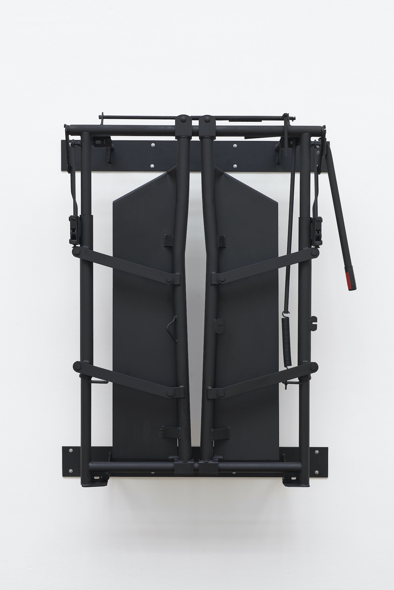 What looks like an industrial sled, or apparatus to restrain animals is painted all black and hangs against a blank white wall