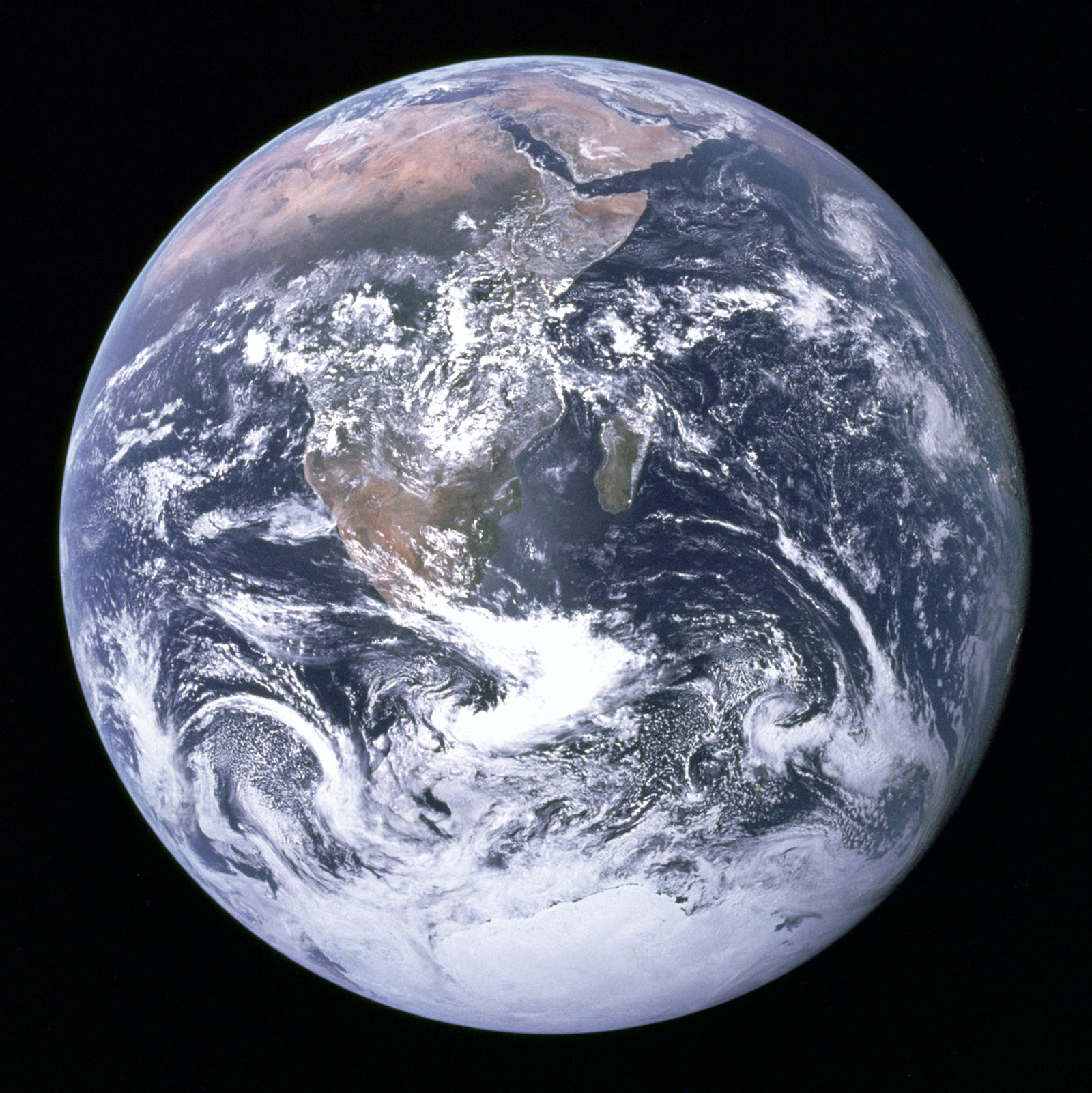 Against the black backdrop of space is the planet Earth, a swirling blue marble of white clouds, blue seas, and dirt colored massive continents.