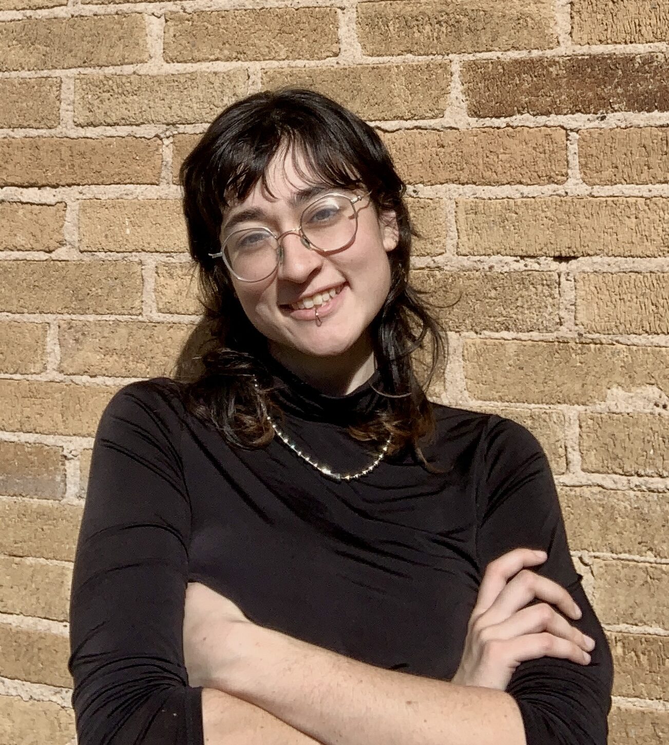 Portrait of a person smiling, wearing glasses and black long sleeve, smiling and arms crossed