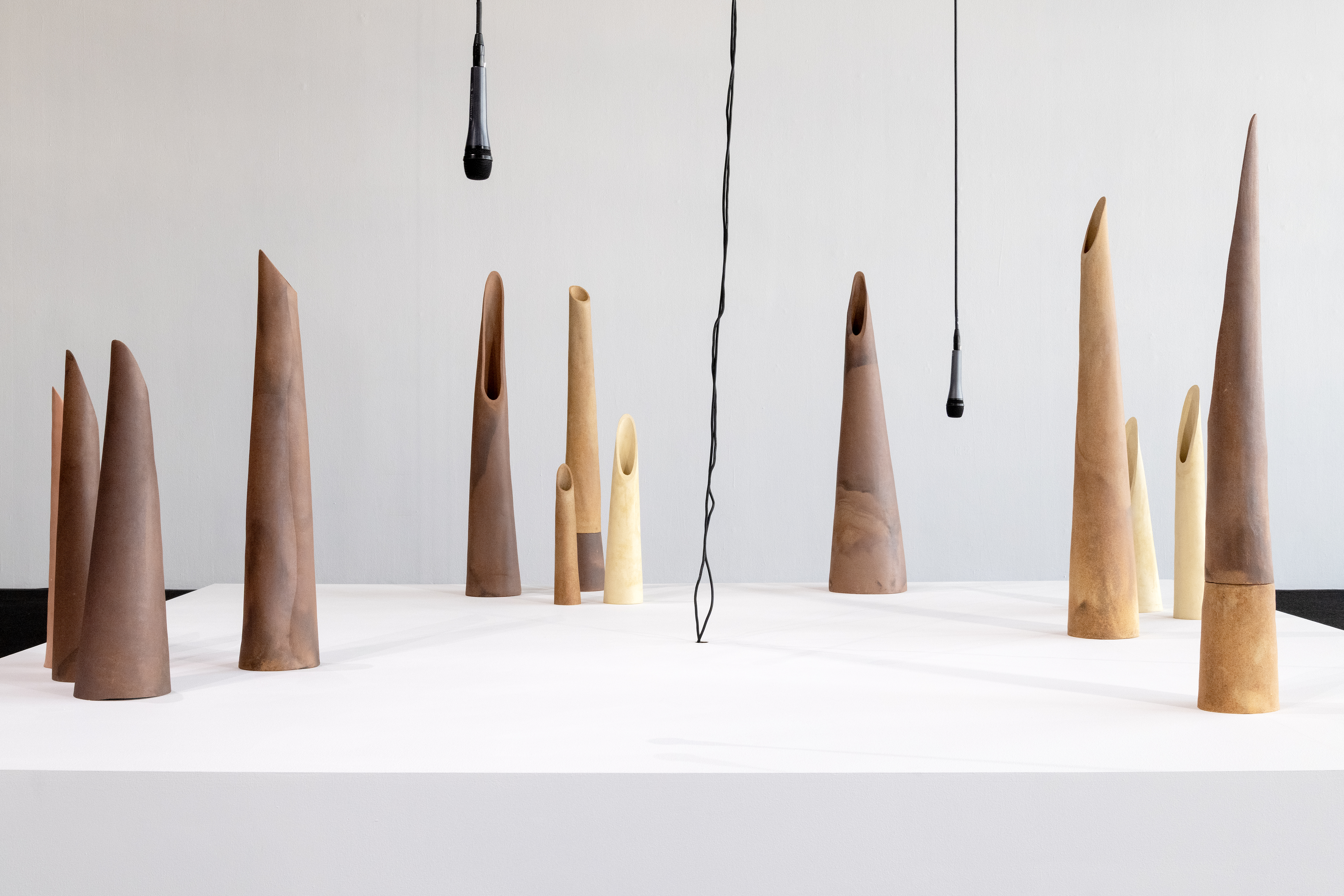 Wooden cones sit on a white platform with microphones hanging down.
