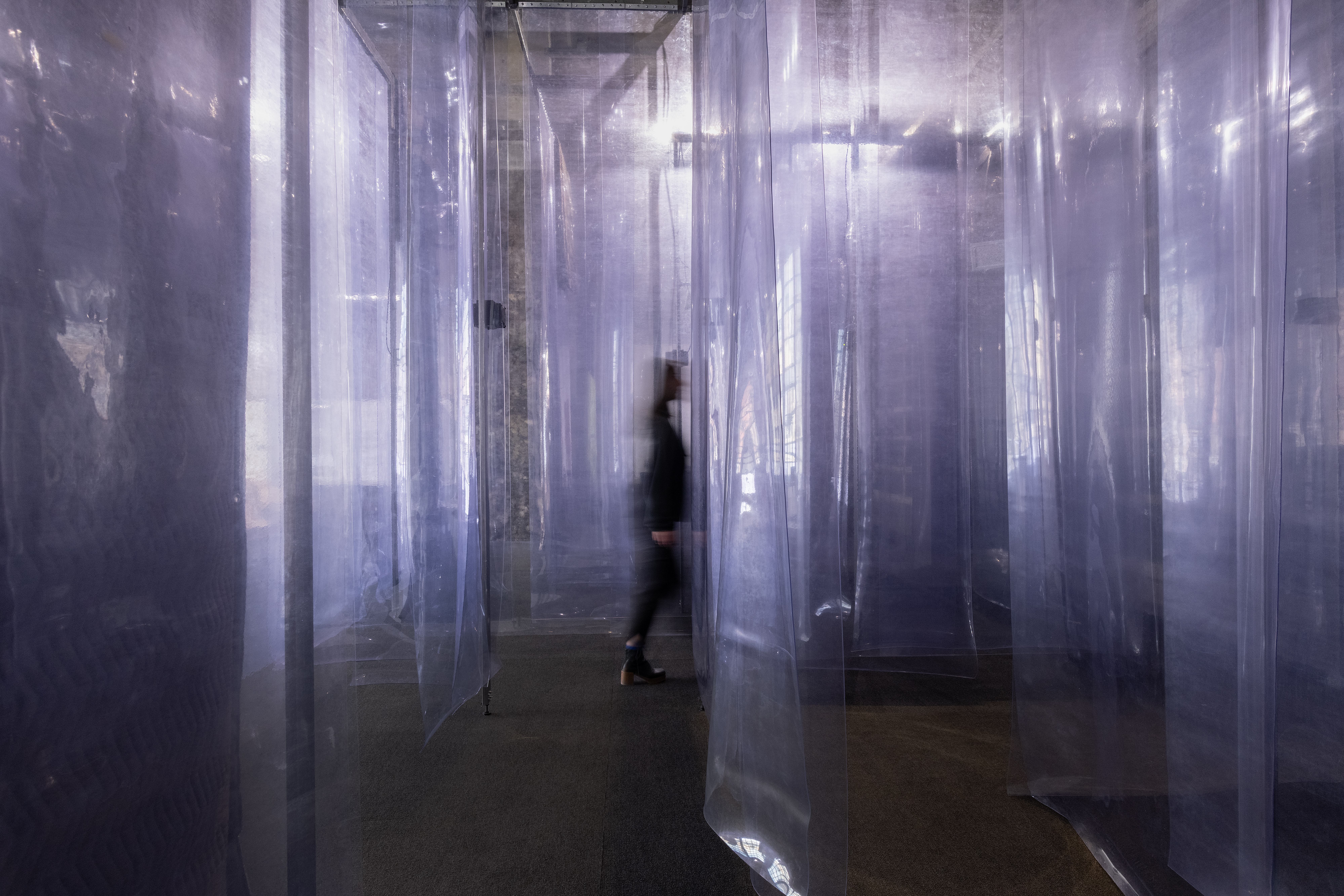 A person walks through sheets of thick plastic hanging from the ceiling to the floor.