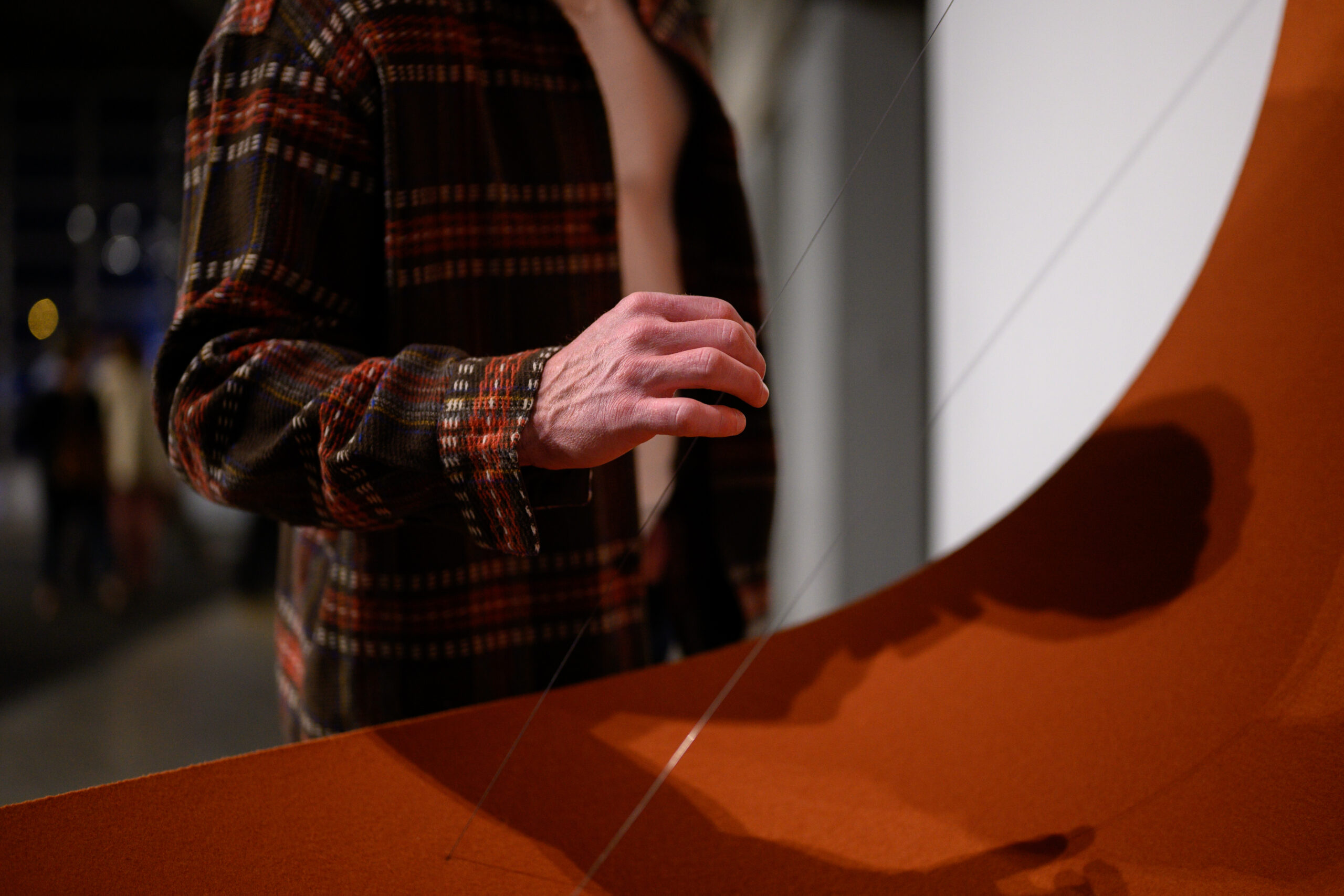 A person interacts with an art piece by placing her hand on a wire that suspends the bottom of an orange material.