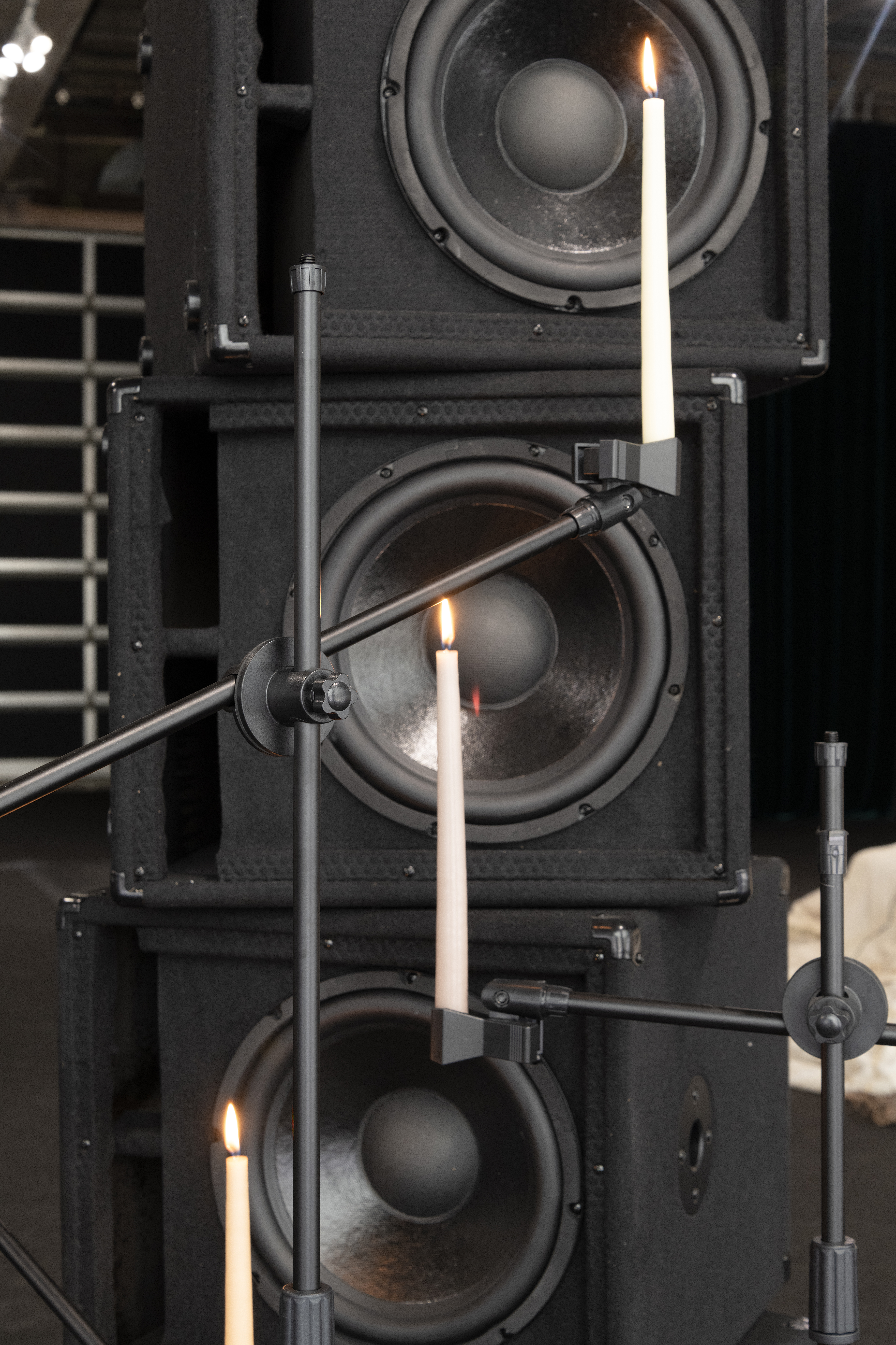 Lit tapered candles are suspended with microphone stands in front of stacked speakers.