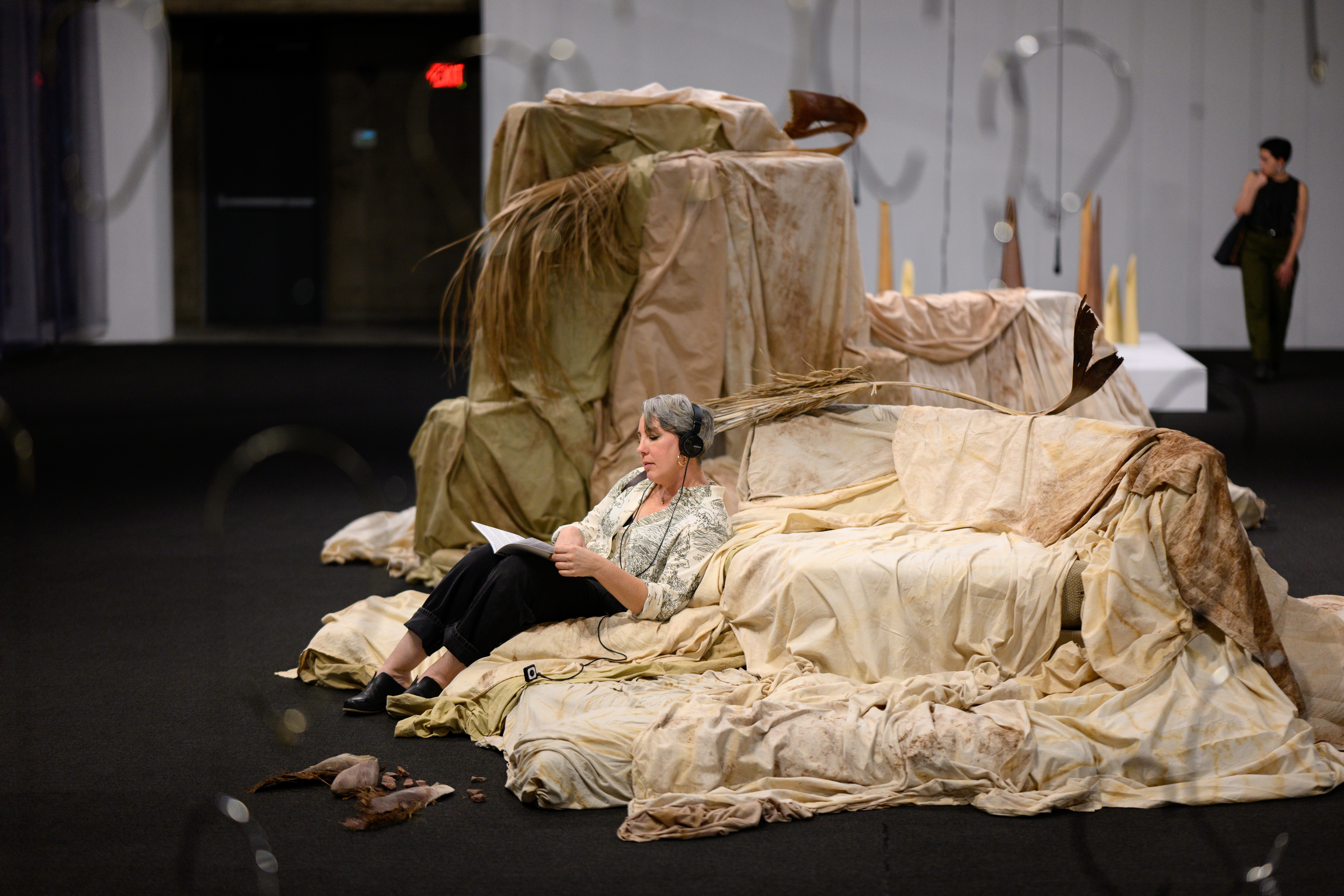 A person sits in an interactive art piece reading with headphones on. The art piece is made with different levels covered in varying tan fabrics.
